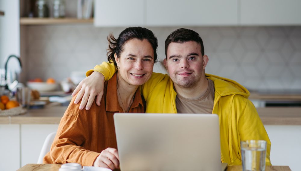 Mom teaching a young man with down syndrome, using laptop. Telehealth consultation with doctor.